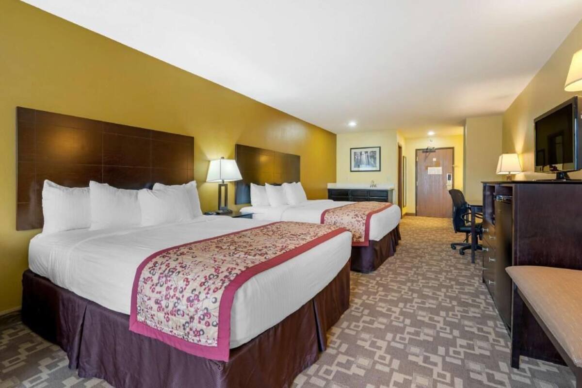 A hotel room with two beds, a desk, a chair, a television, and a door.