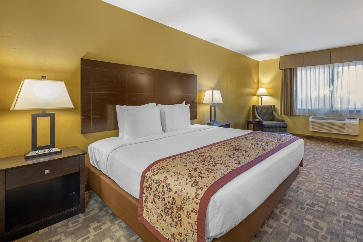 A hotel room with a large bed, two bedside lamps, a chair, and a window with curtains.