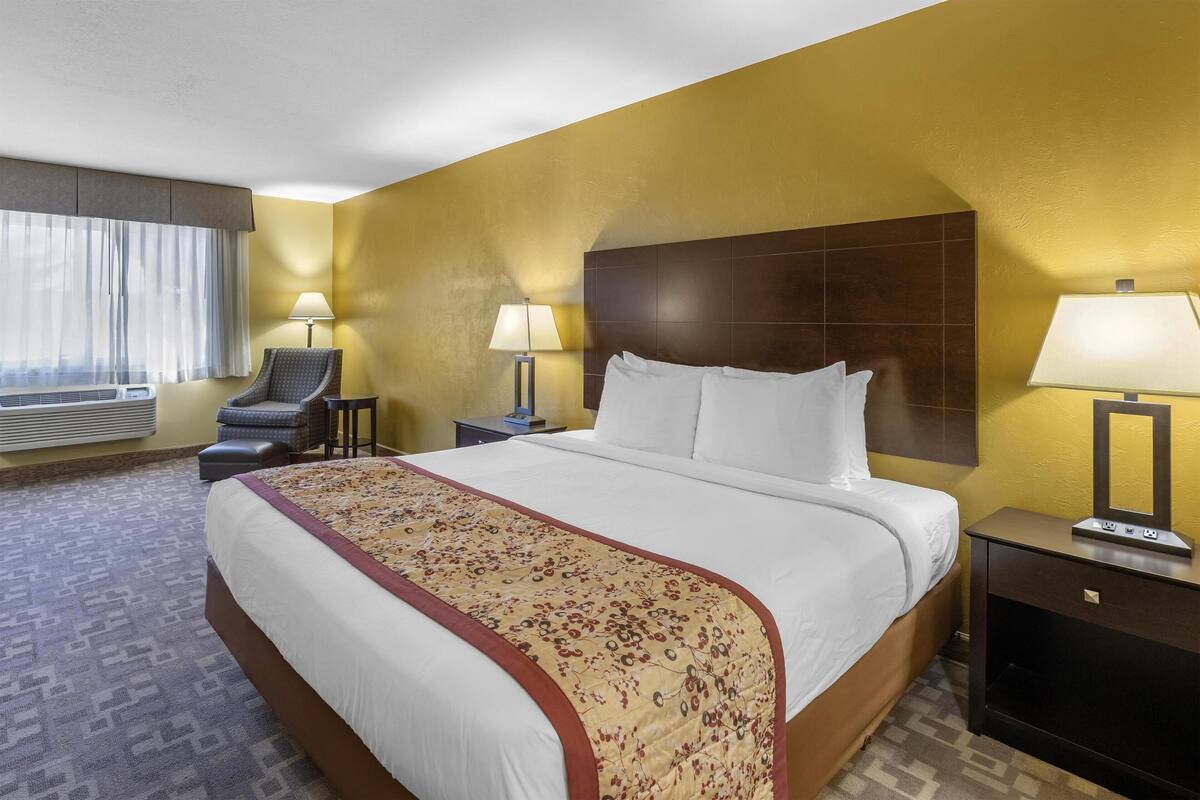 A hotel room with a large bed, two bedside lamps, a chair, and a nightstand.