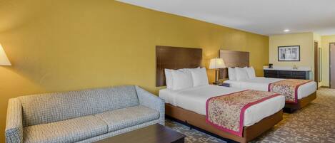 A hotel room with a sofa, two beds, a small table, and a patterned carpet.