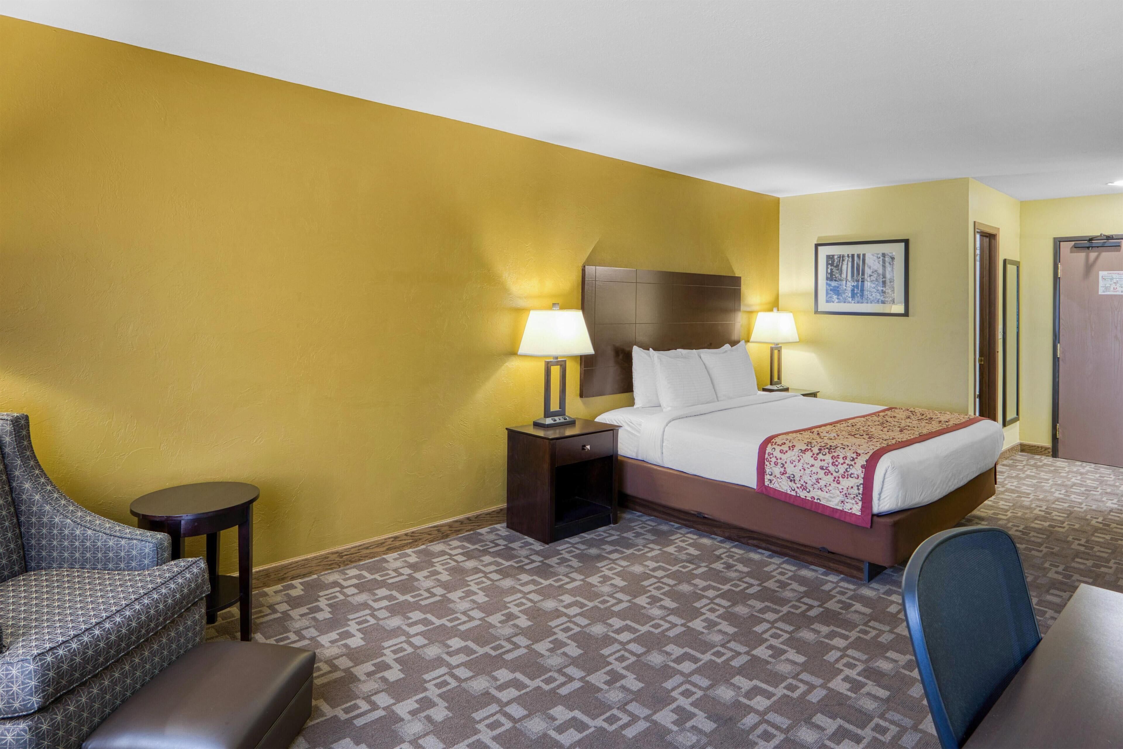 A hotel room with a bed, two bedside tables with lamps, a chair, and a patterned carpet.