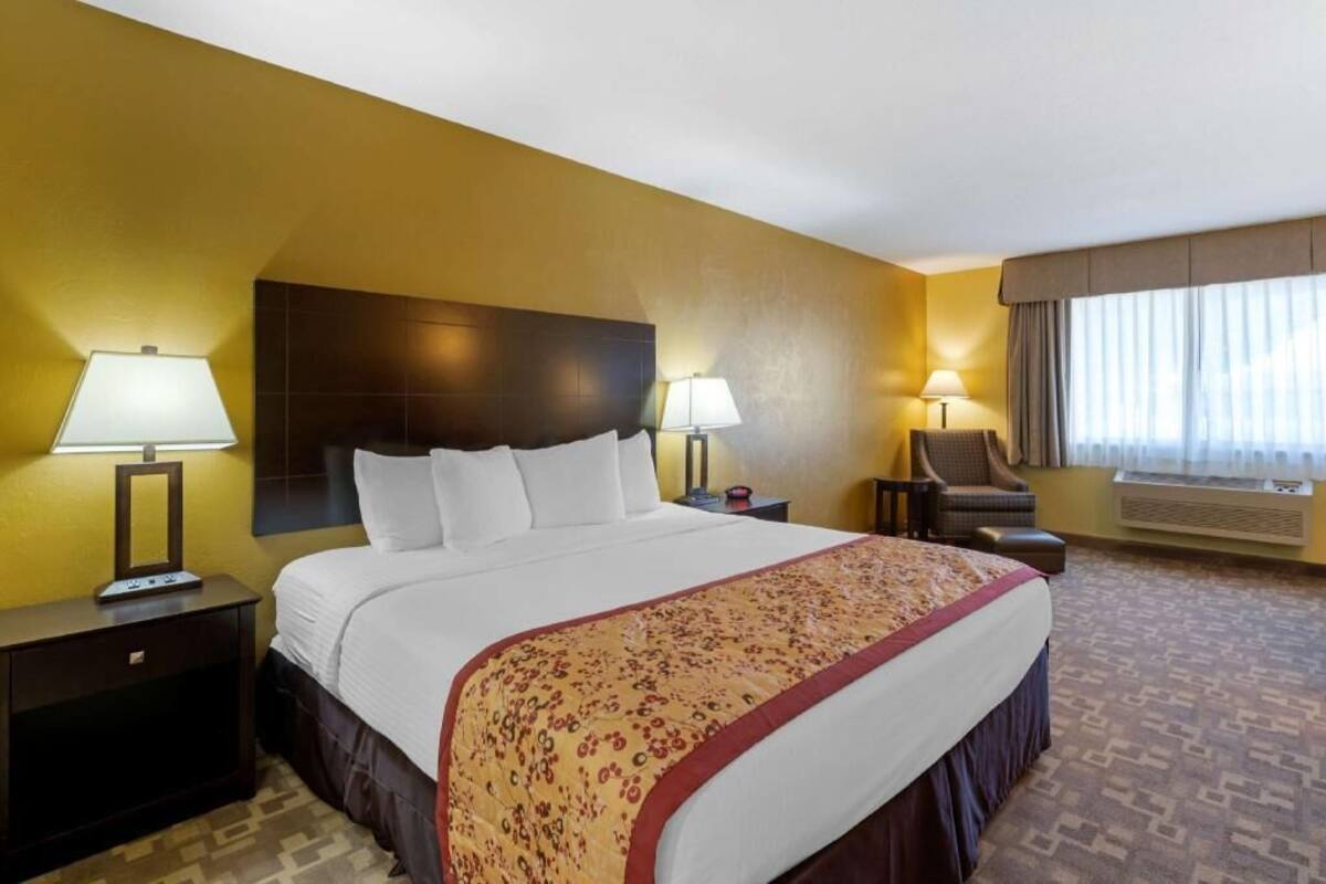 A hotel room with a large bed, two bedside tables with lamps, a chair, and a window with curtains.