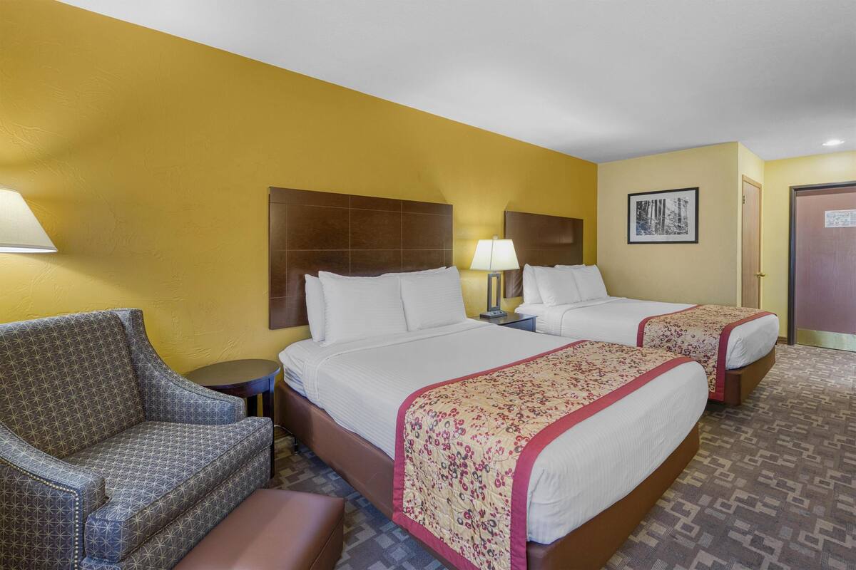A hotel room with two beds, a sofa, a nightstand, and a lamp.