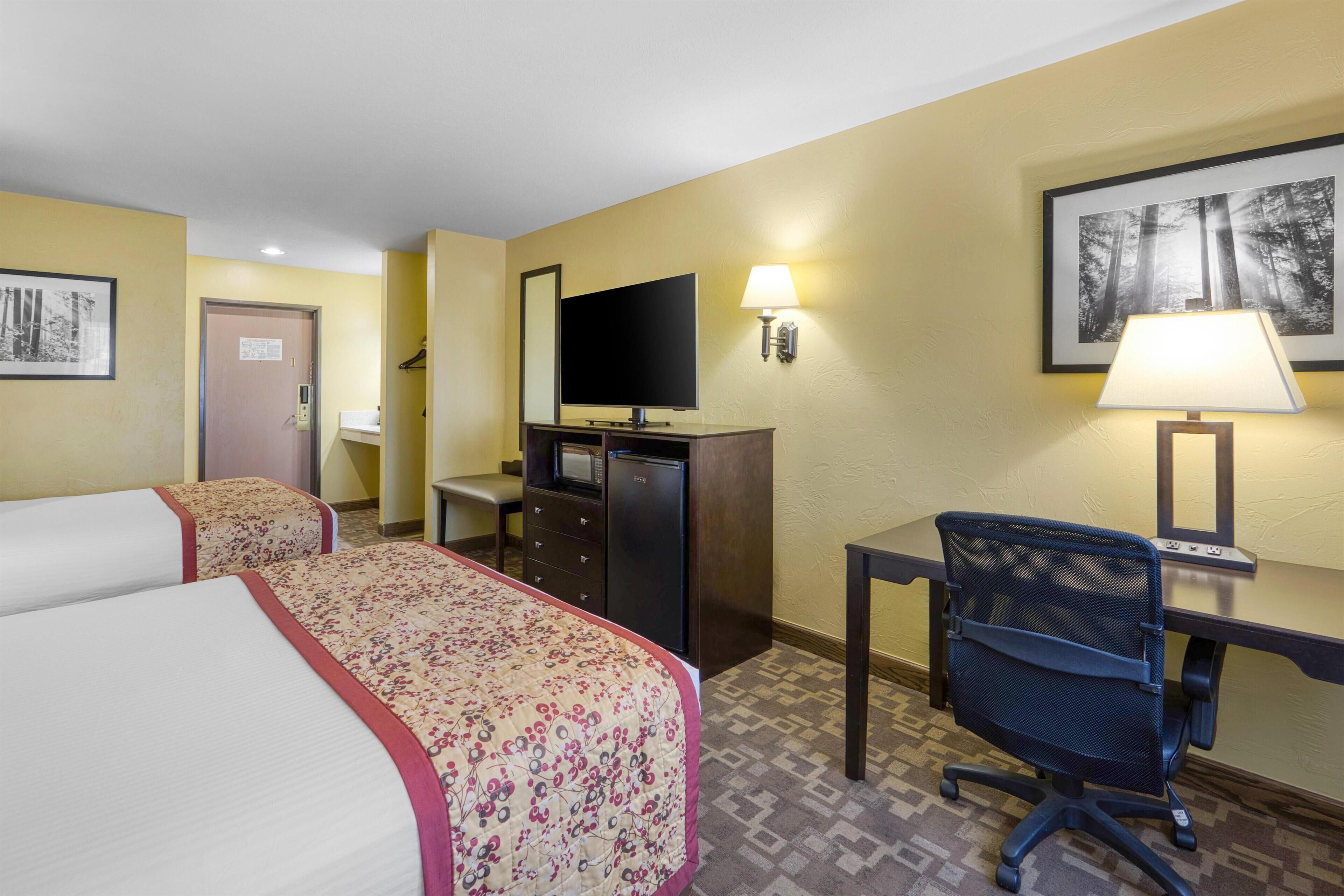 Una camera d'albergo con due letti, una scrivania, una sedia, una televisione e una lampada.