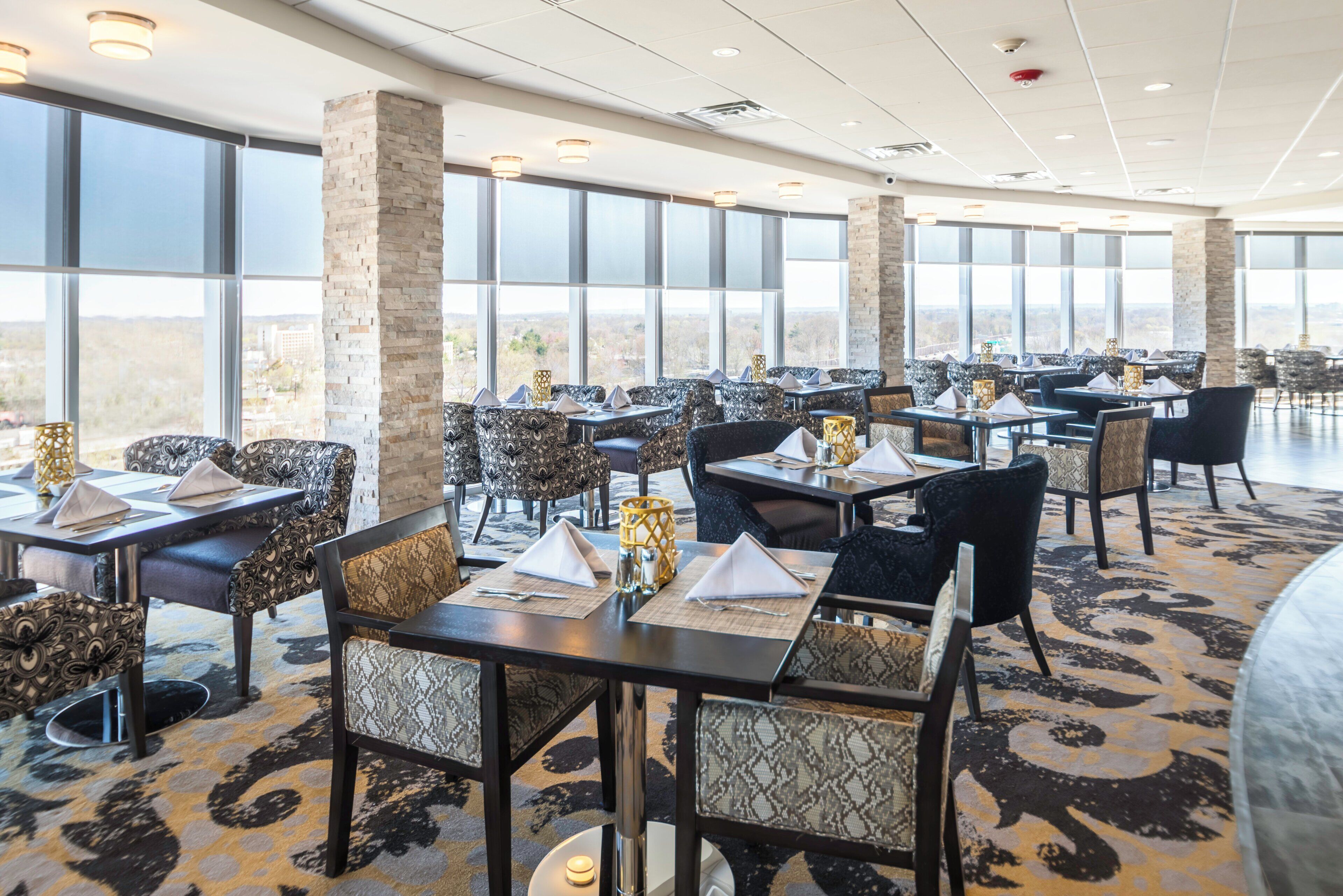 A spacious dining area with multiple tables and chairs, large windows, and a view of the landscape.