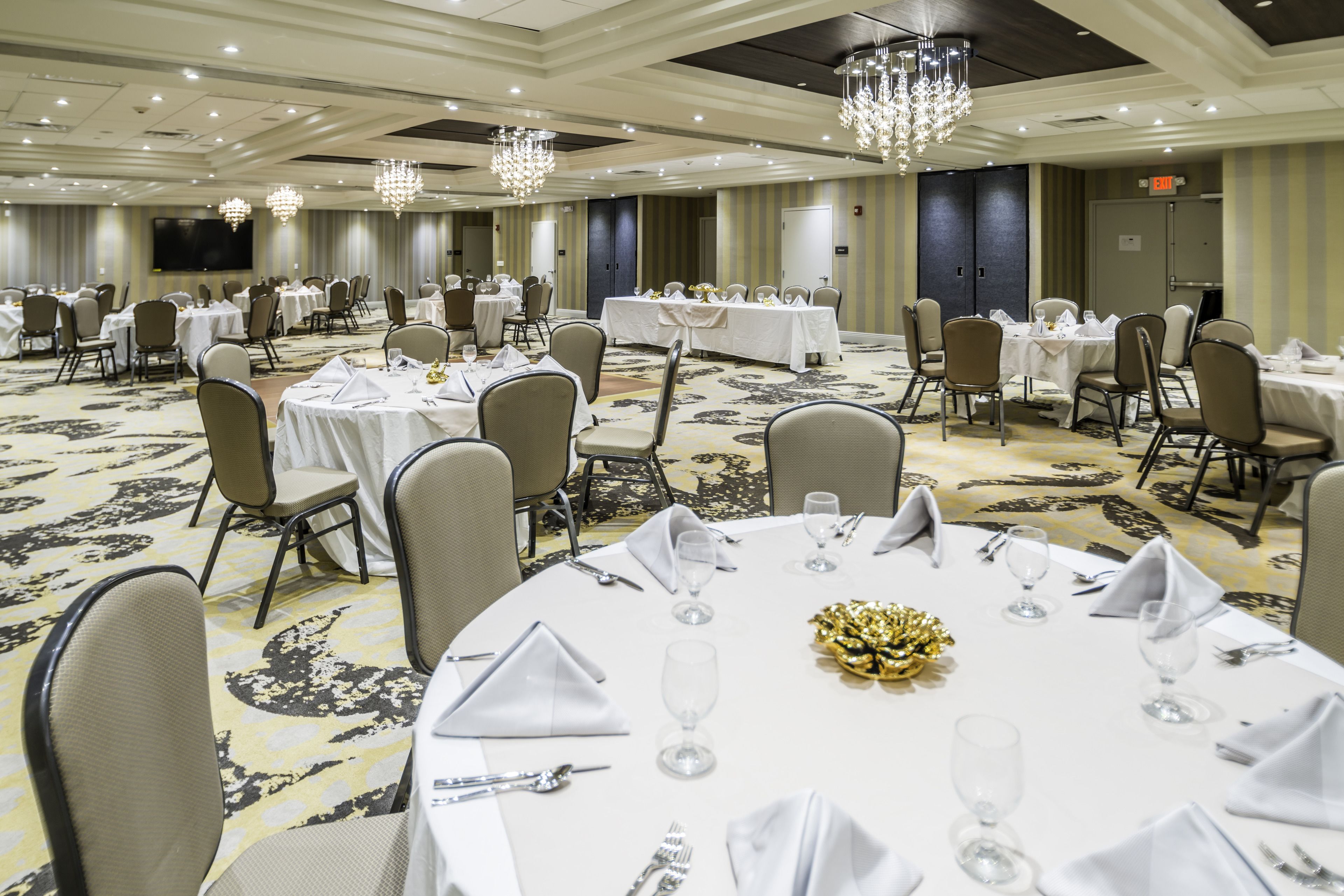A banquet hall with round tables set for dining, each with white tablecloths, chairs, and glassware.