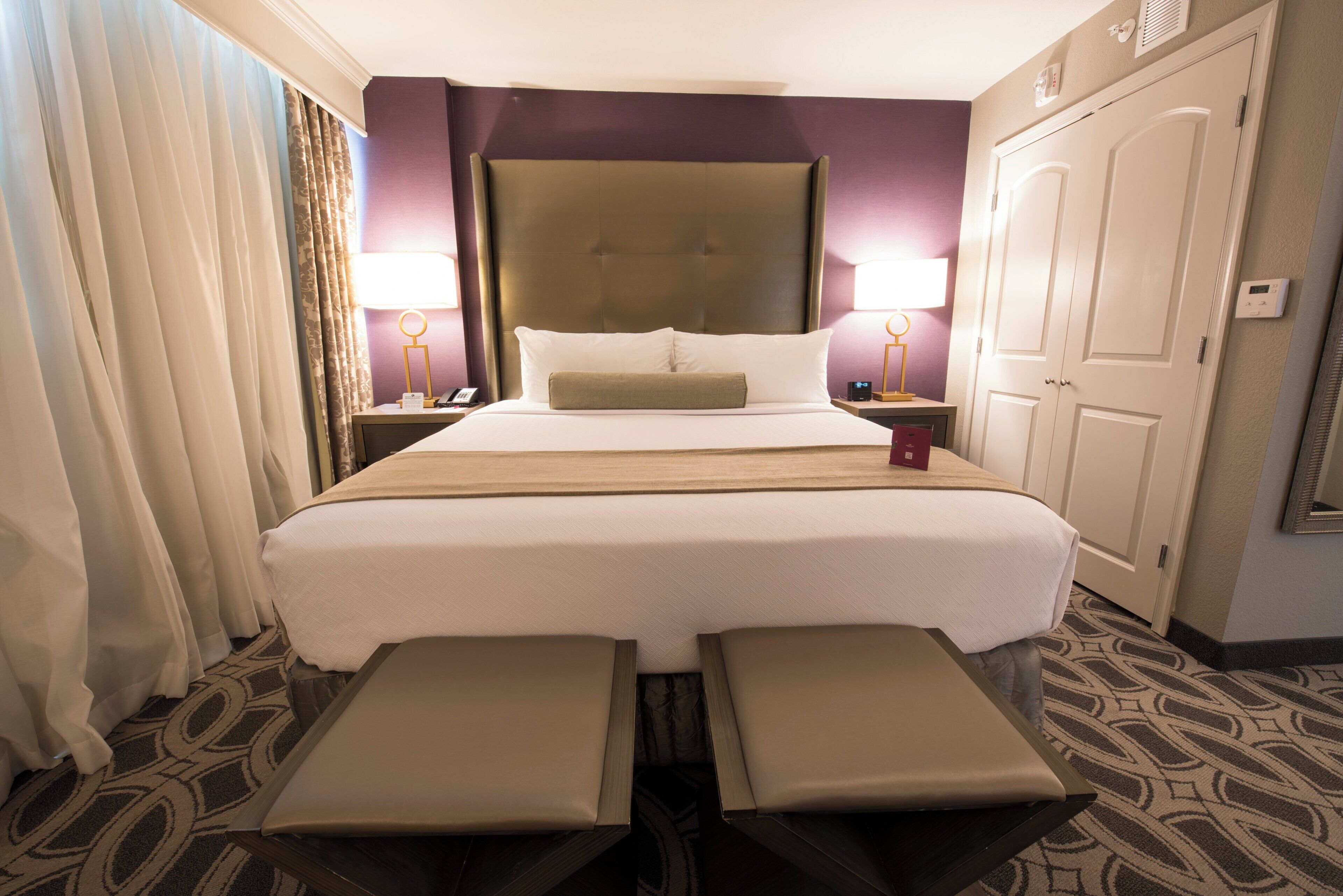 A hotel room with a large bed, bedside lamps, a wardrobe, and a bench at the foot of the bed.