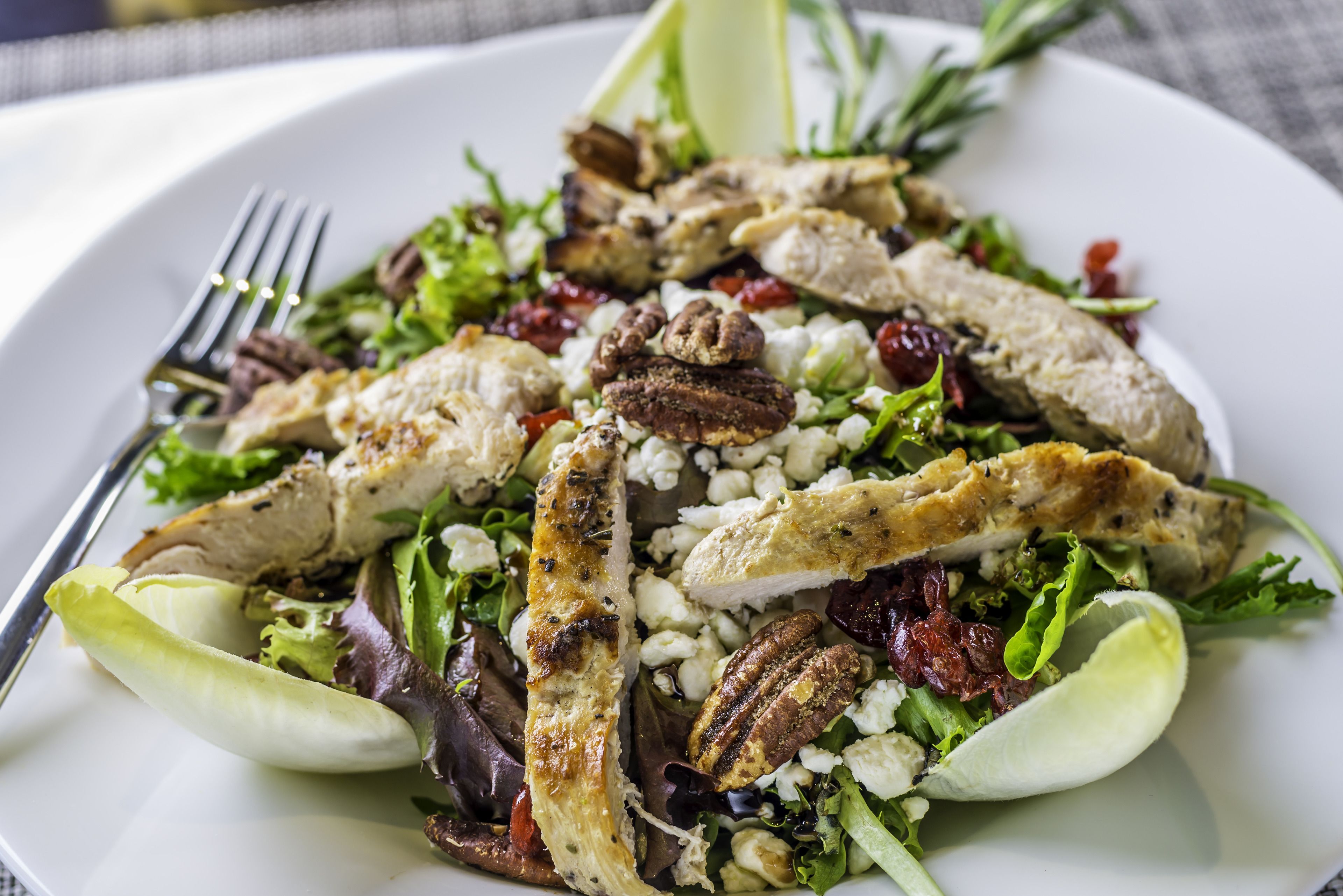 A plate of food with grilled chicken, nuts, and greens.