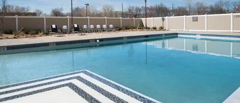A swimming pool with a tiled edge, lounge chairs, and a fence.