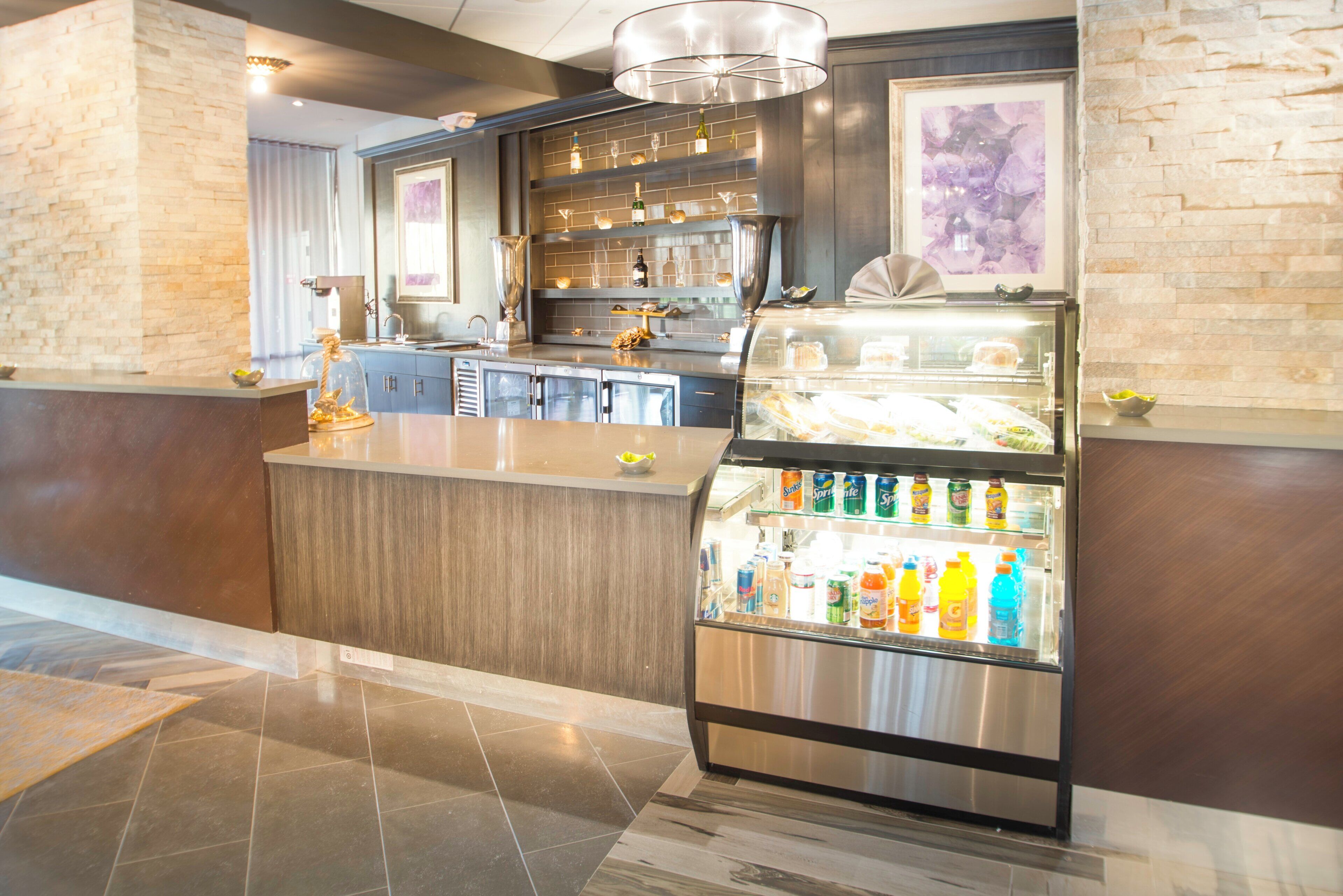 A hotel lobby with a bar area, a refrigerated display case with beverages, and a decorative wall with a framed picture.