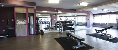 A gym with exercise equipment, mirrors, and a weight rack.