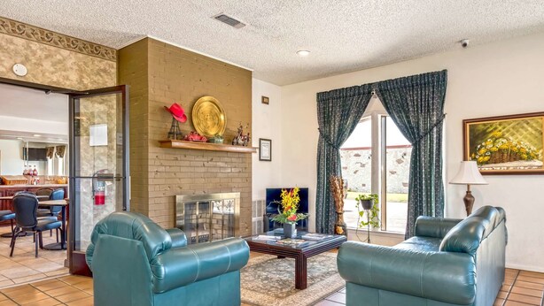 A living room with two blue leather sofas, a fireplace, a television, and a dining area visible through an open door. - Americas Best Value Inn Paris (Paris)