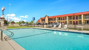 A swimming pool with lounge chairs and a motel building in the background.