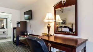 A hotel room with a desk, two lamps, a mirror, a television, and a bed. - Americas Best Value Inn Paris (Paris)