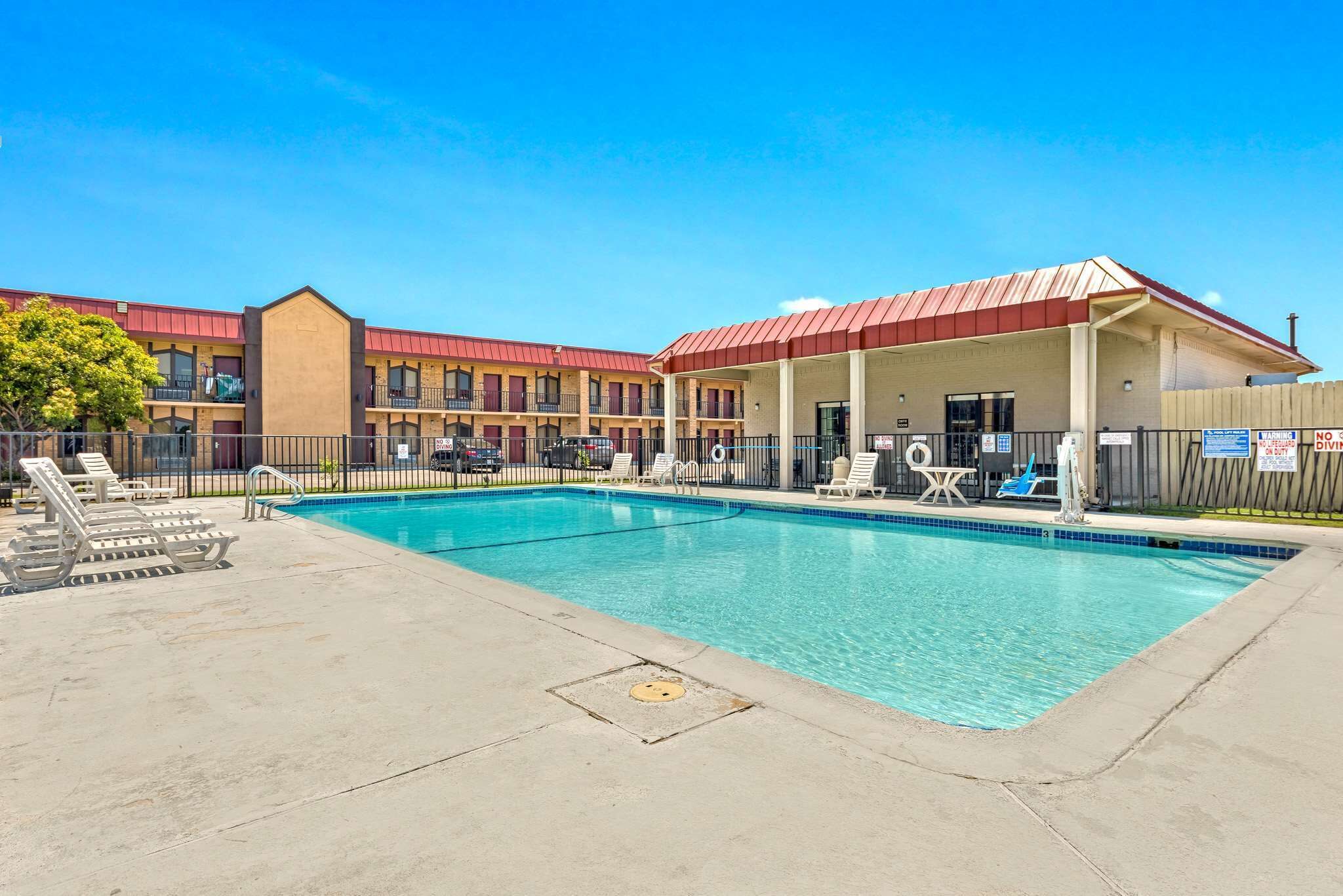 A hotel with a swimming pool, outdoor seating, and a covered area with tables and chairs.