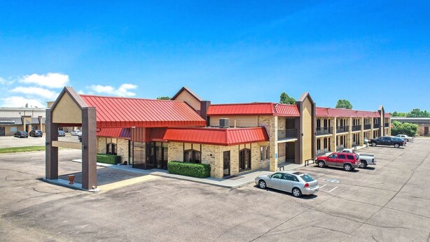 A multi-story motel with red roofs and brick exteriors, featuring a parking lot with several cars.