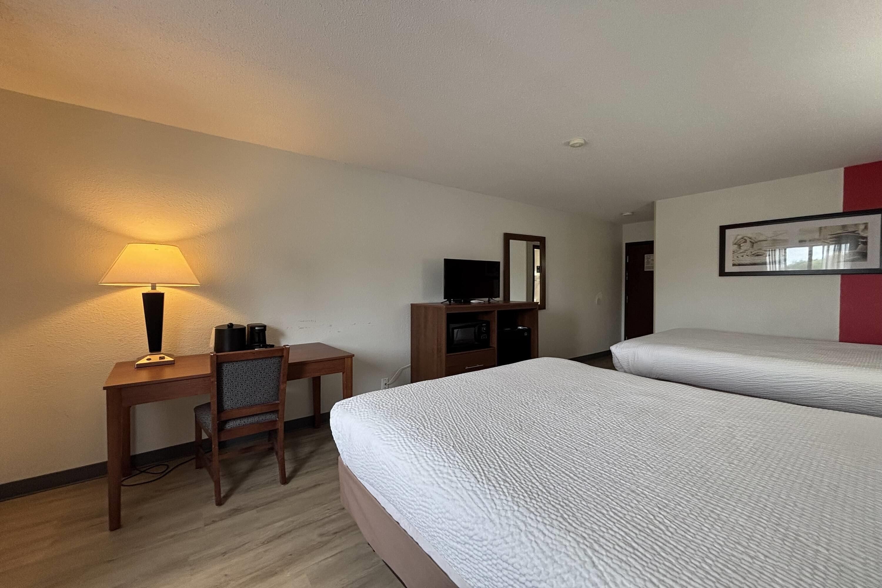 A hotel room with two beds, a desk with a lamp, a TV, and a microwave.