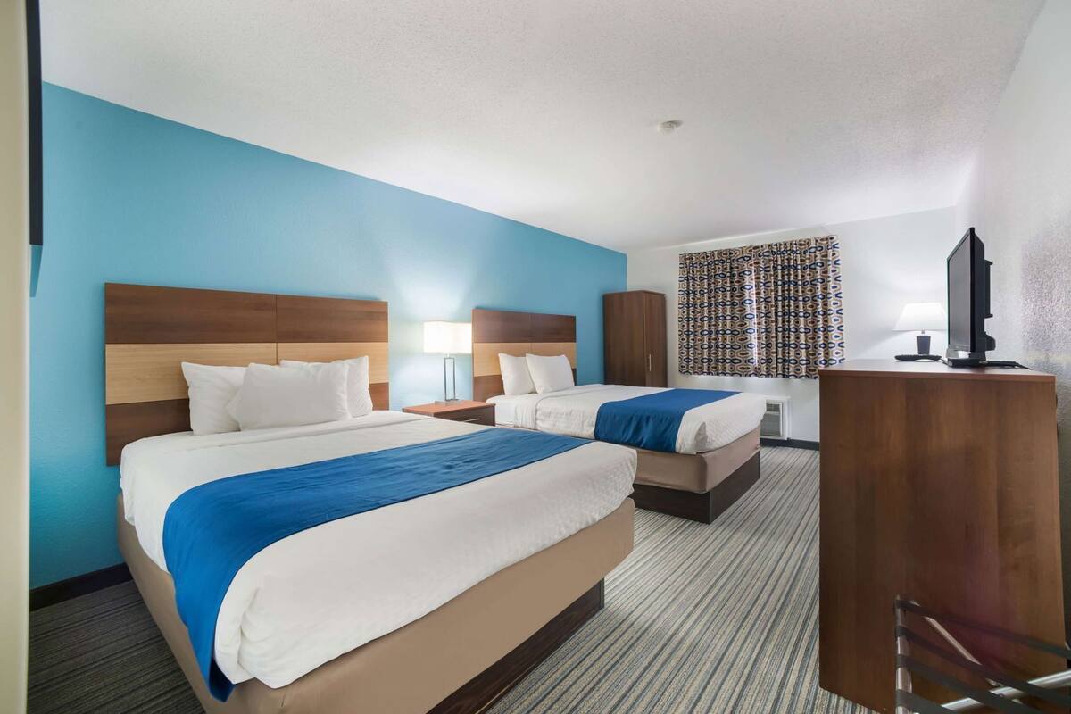 A hotel room with two beds, a desk, a TV, and a patterned curtain.