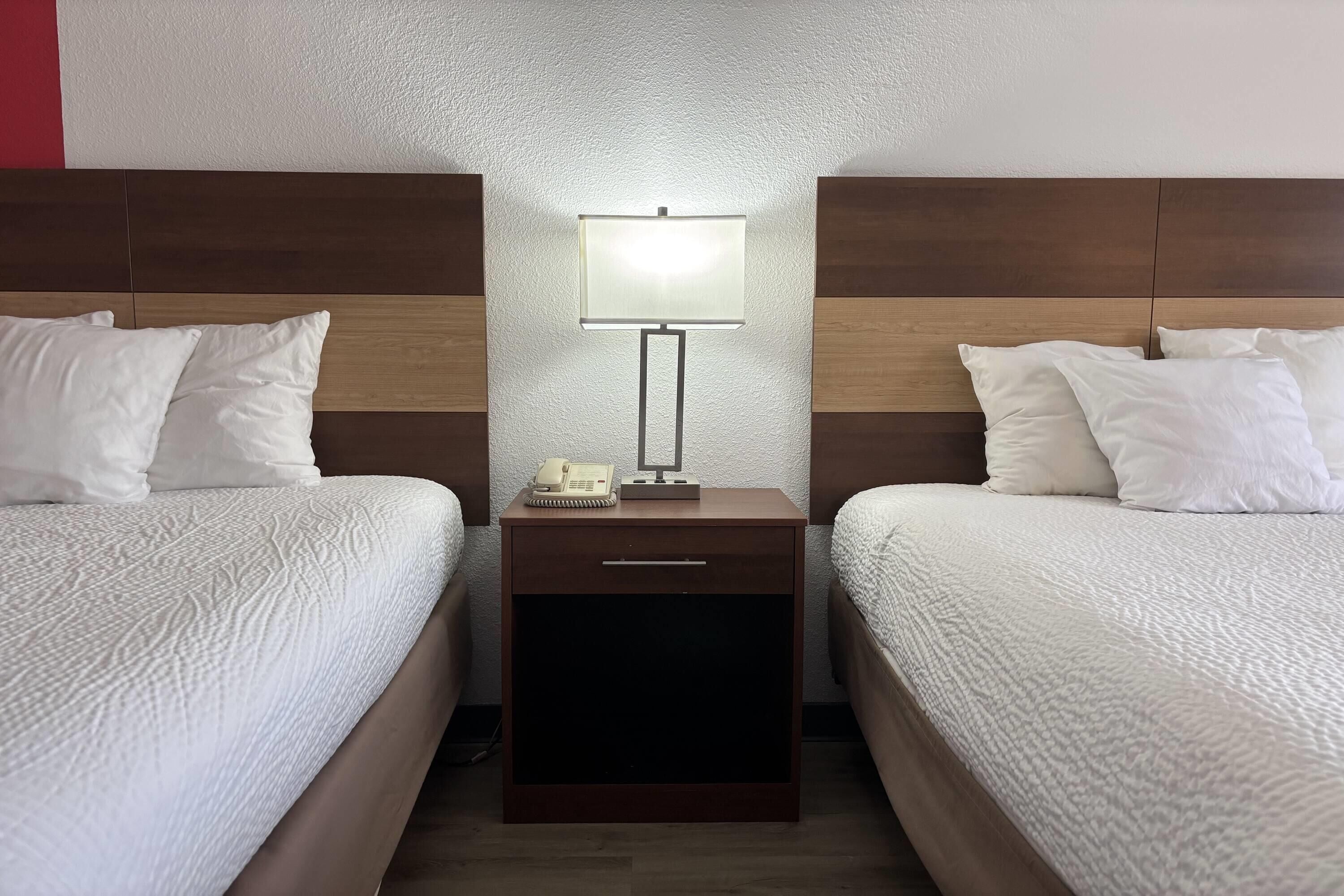 Una habitación de hotel con dos camas, una mesita de noche con lámpara y teléfono.