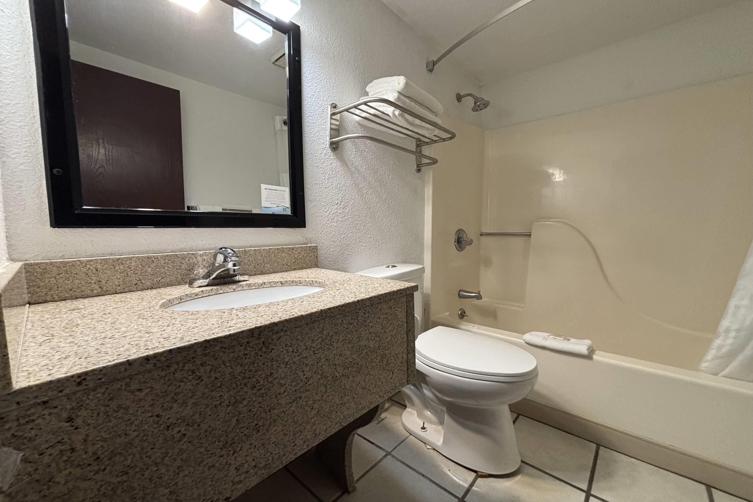 A bathroom with a granite countertop sink, a white toilet, a bathtub, and a towel rack.