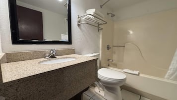 A bathroom with a granite countertop sink, a white toilet, a bathtub, and a towel rack.