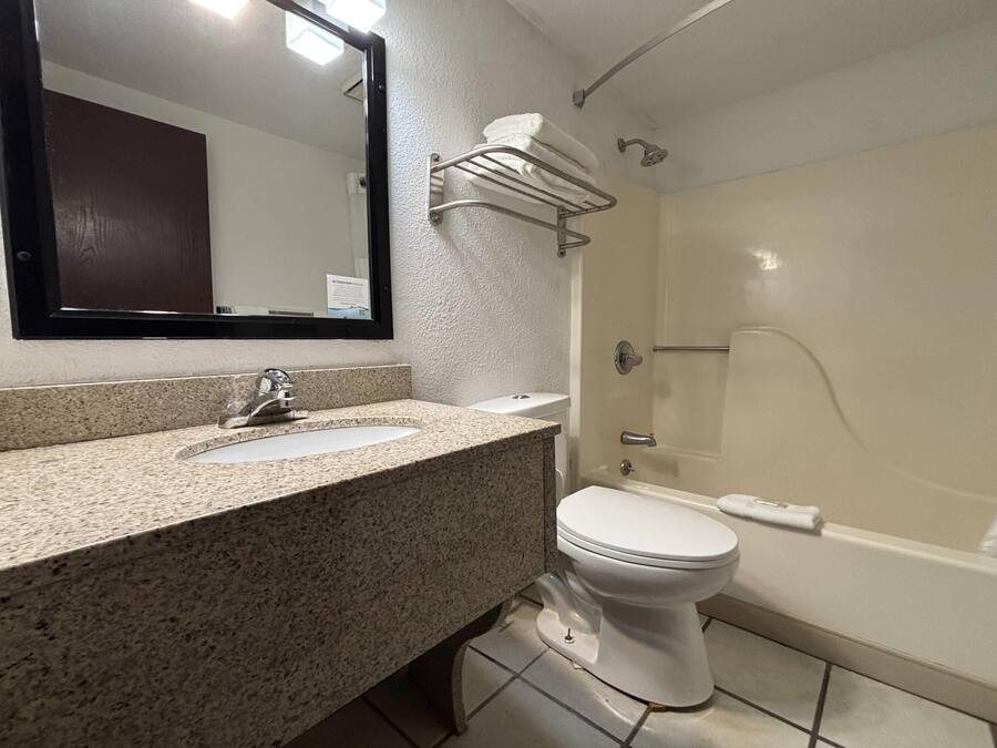 A bathroom with a granite countertop sink, a white toilet, a bathtub, and a towel rack.