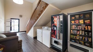 A hotel room with a sofa, a washing machine, a vending machine, and a staircase.