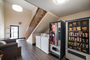 A hotel room with a sofa, a washing machine, a vending machine, and a staircase. - Ramada by Wyndham Effingham (Effingham)