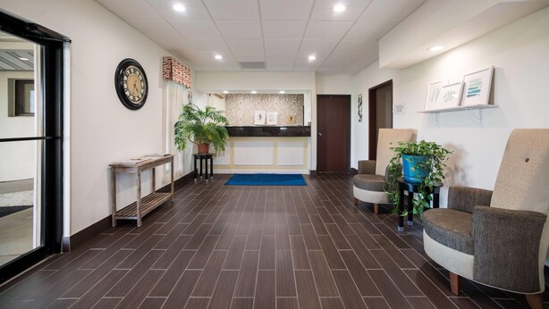 A reception area with a reception desk, a clock, a blue mat, and two potted plants.