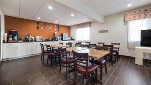 A dining area with a central table surrounded by chairs, a kitchen area with appliances, and a sign that reads 'Coffee Anyone?'