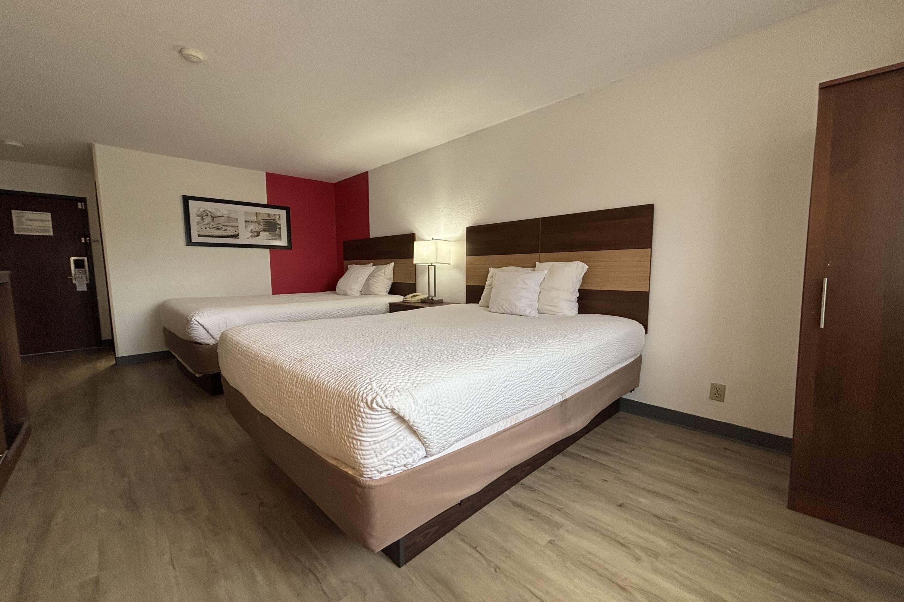 Une chambre d’hôtel avec deux lits, une tête de lit en bois, une lampe de chevet et un mur d’accent rouge.