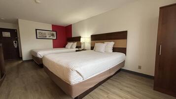 Une chambre d’hôtel avec deux lits, une tête de lit en bois, une lampe de chevet et un mur d’accent rouge.