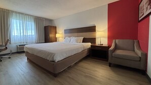 A hotel room with a bed, bedside tables, a chair, and a window with curtains.