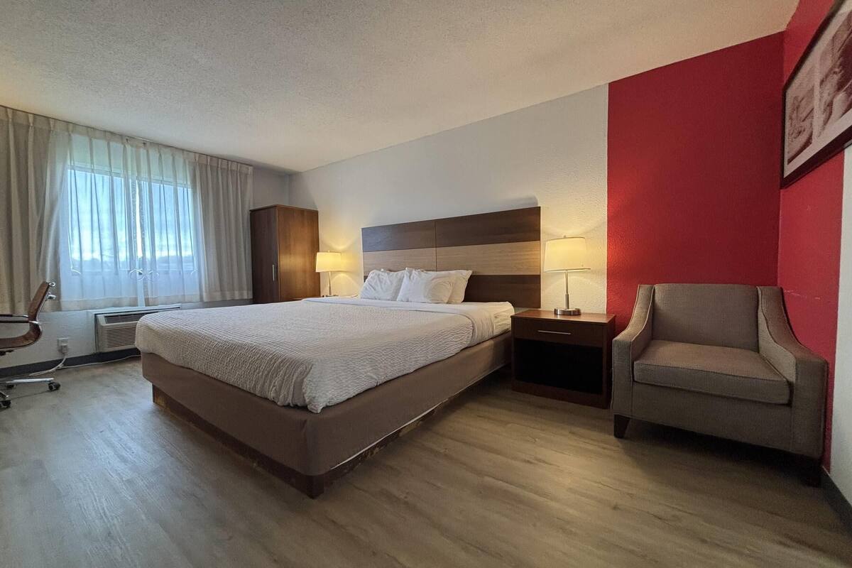 A hotel room with a bed, bedside tables, a chair, and a window with curtains.