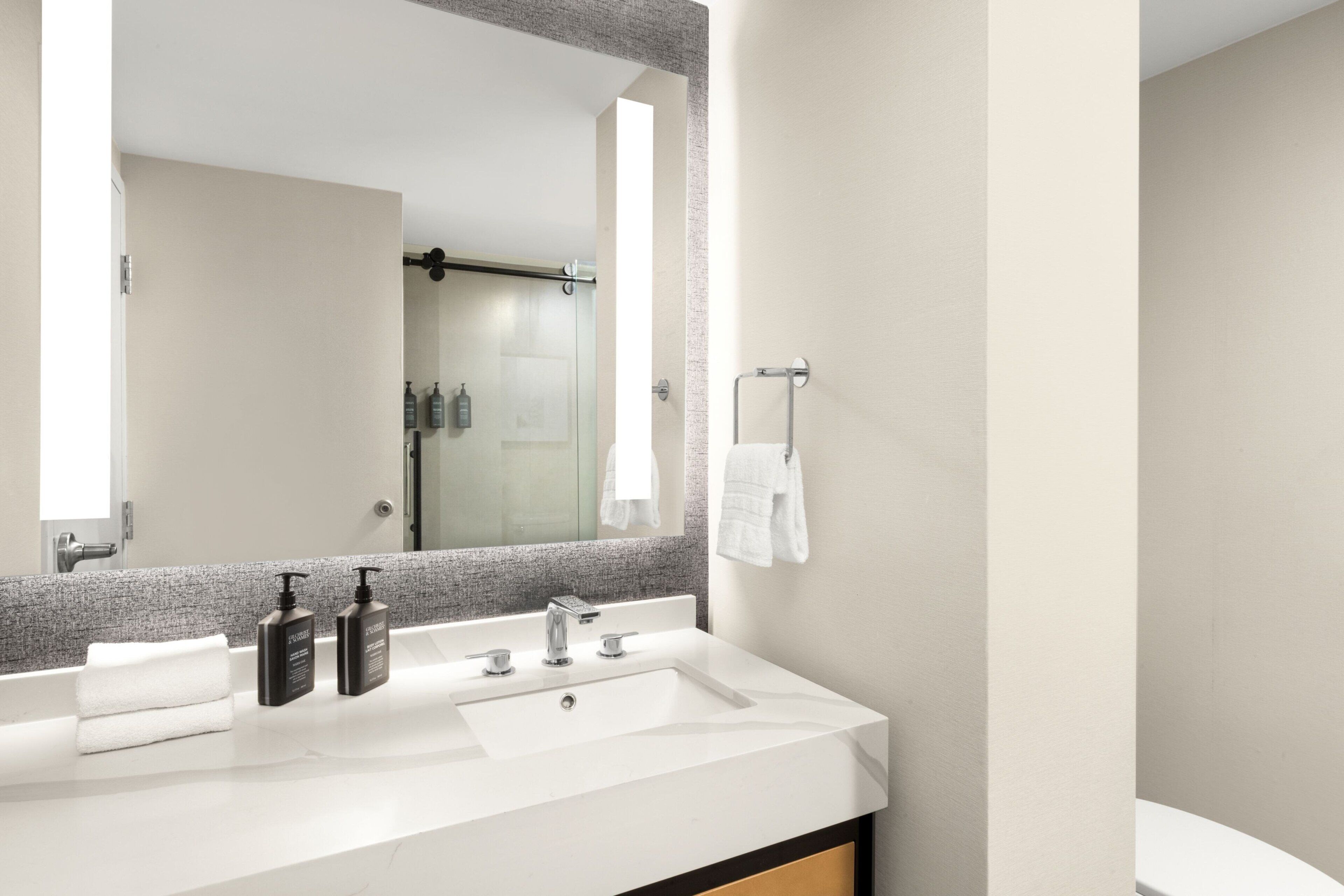 Un baño moderno con un espejo grande, un lavabo blanco y dos botellas de champú.