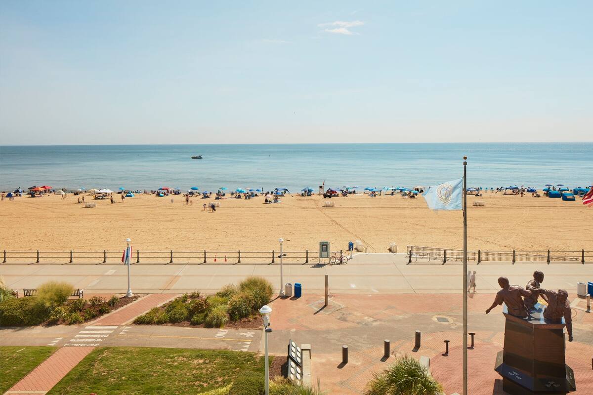 A beach with a paved walkway, benches, and a statue.