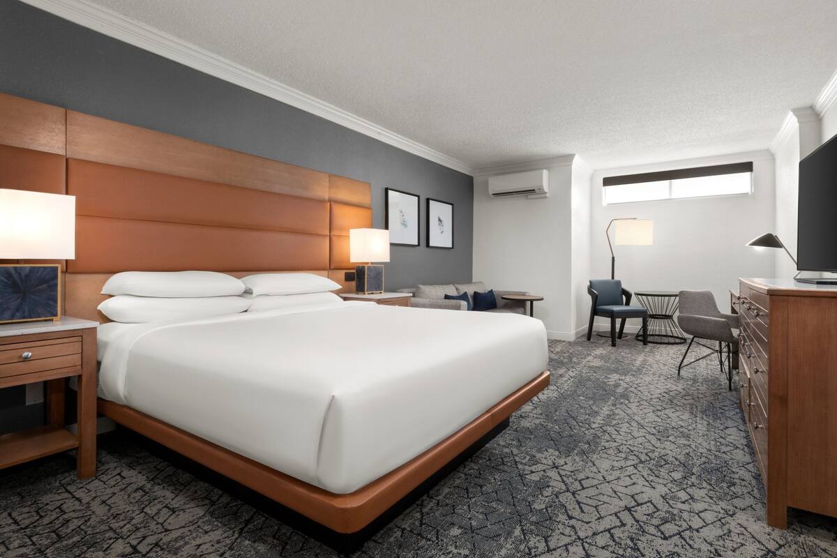 A hotel room with a large bed, bedside tables, a desk, a chair, and a TV.
