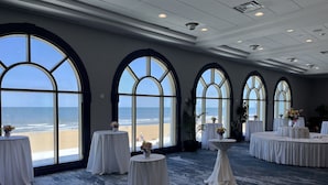 Ein Zimmer mit großen Bogenfenstern mit Blick auf einen Strand, ausgestattet mit weißen Tischen und Stühlen.