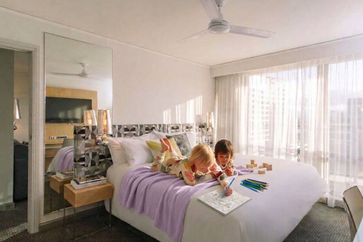 Quarto de hotel com cama, mesa de cabeceira, espelho, ventilador de teto e janela com cortinas.