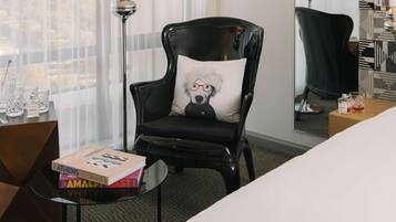 A hotel room with a black leather armchair, a small round table with books, and a large bed.