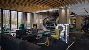 A modern lobby with a curved staircase, a seating area with sofas and a round table, and a large illuminated 'OT' sign. - QT Canberra (Canberra)