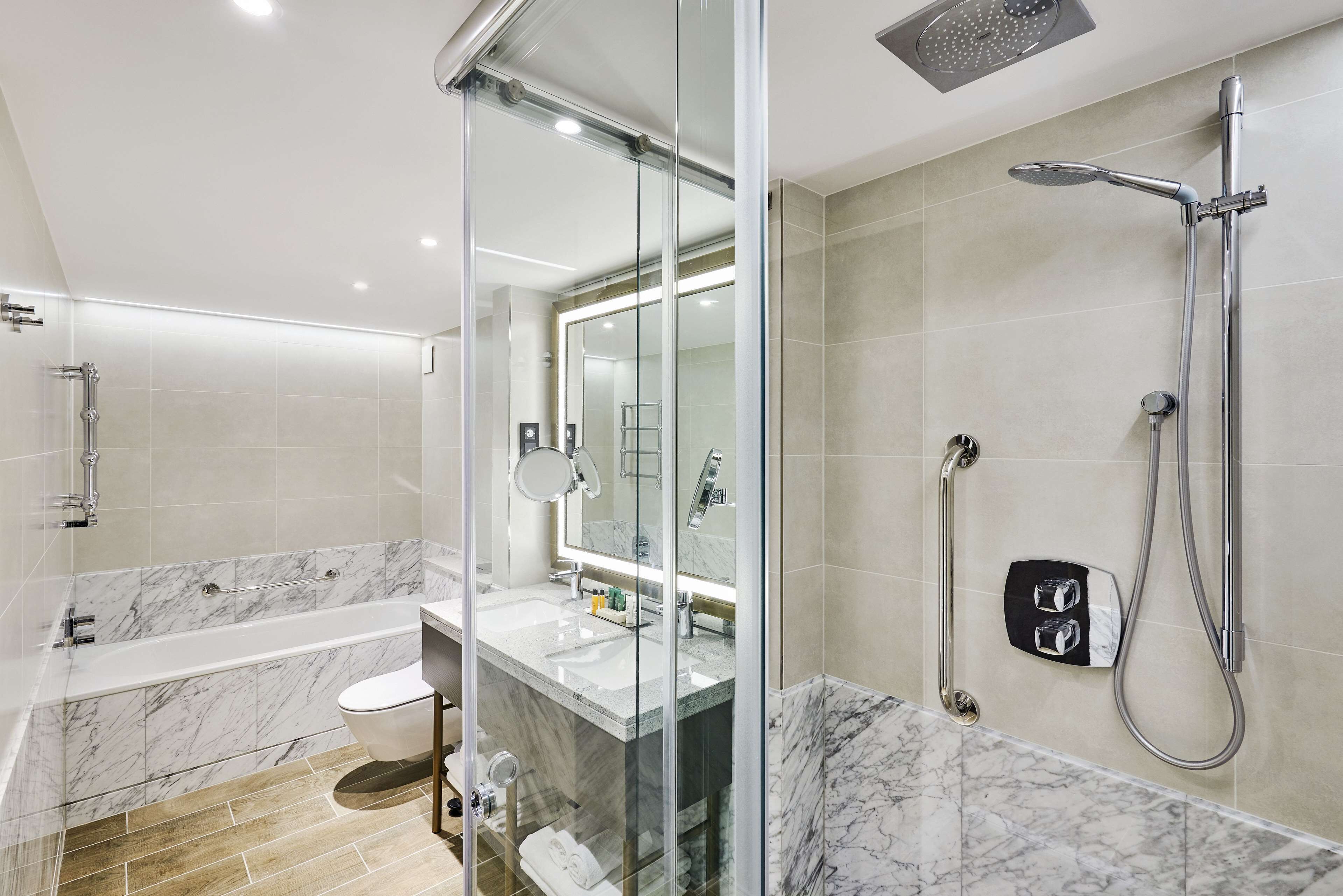 Un baño moderno con ducha de vidrio, bañera separada y tocador con espejo.