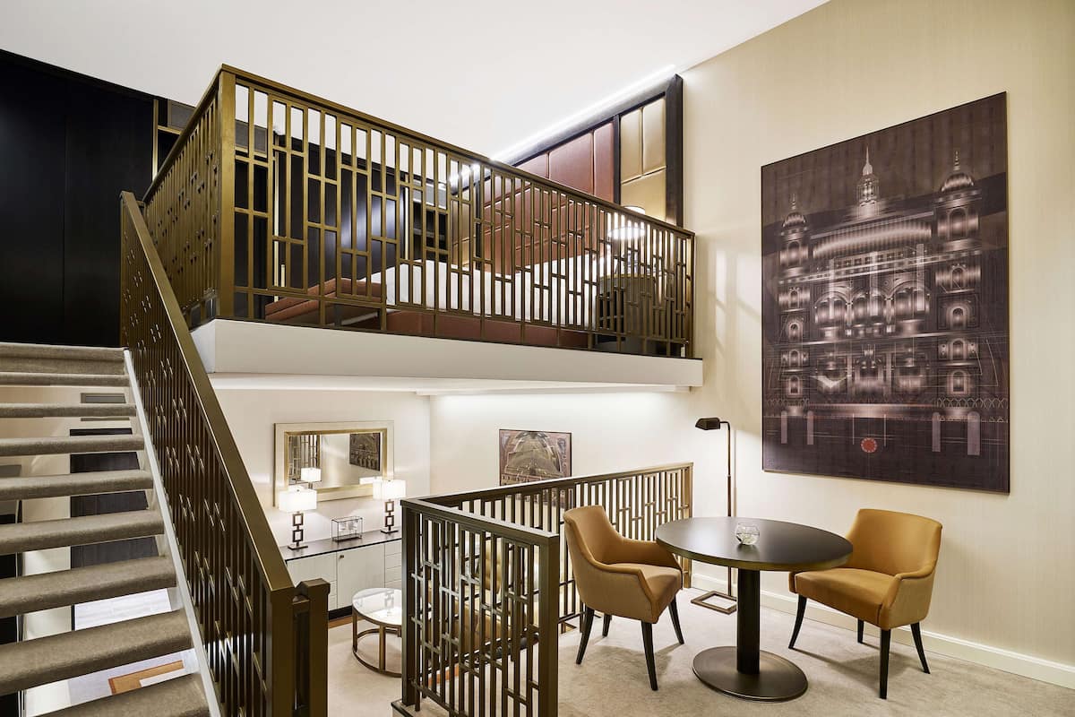 Un intérieur à deux niveaux avec un escalier, un coin repas comprenant des chaises et une table, et un grand tableau encadré accroché au mur.
