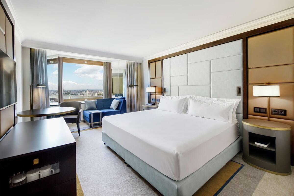 Une chambre d’hôtel avec un grand lit, un bureau, une chaise, un canapé et une vue sur la ville.