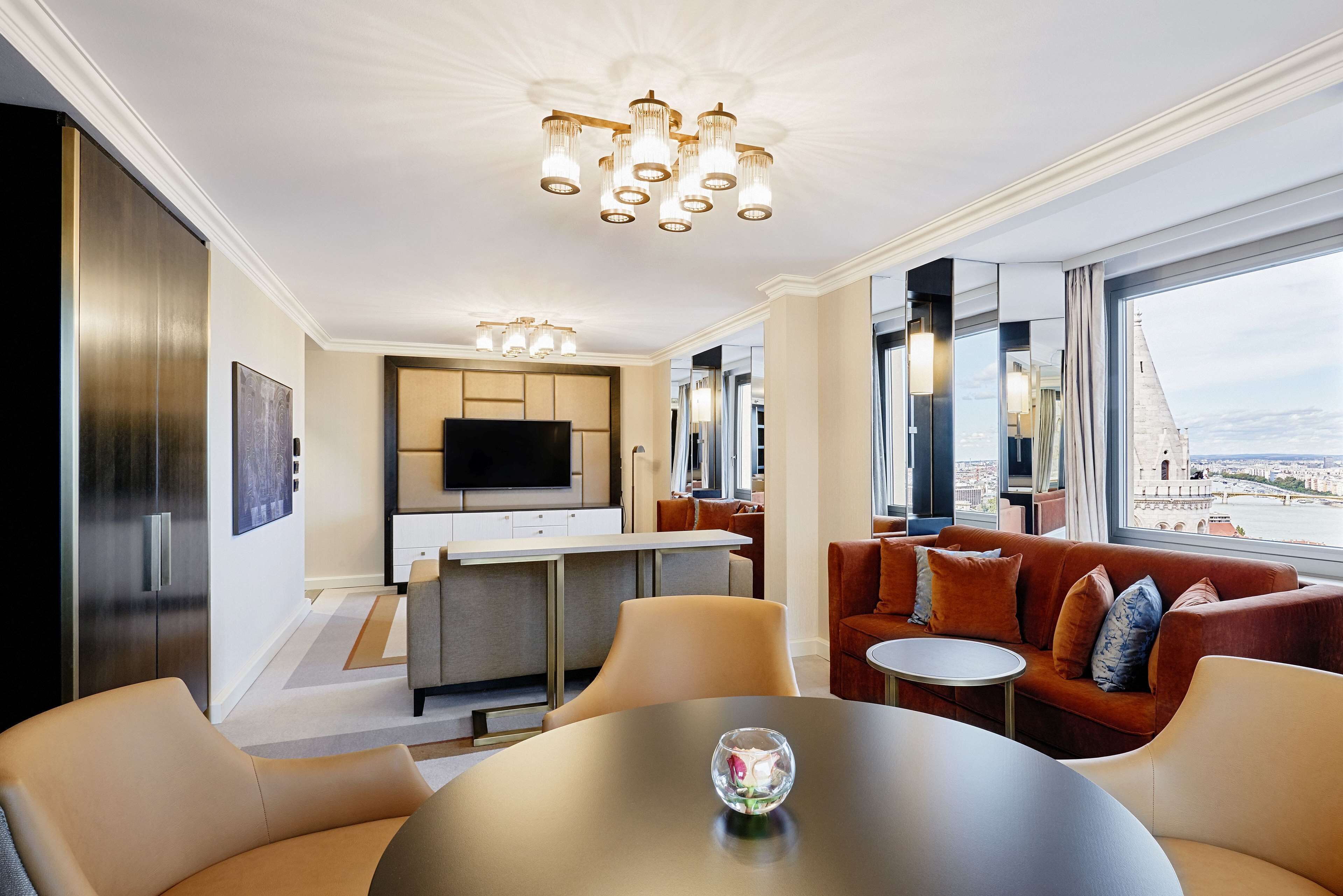 Une chambre d’hôtel moderne dotée d’un coin repas, d’un canapé et d’une grande fenêtre donnant sur la ville.