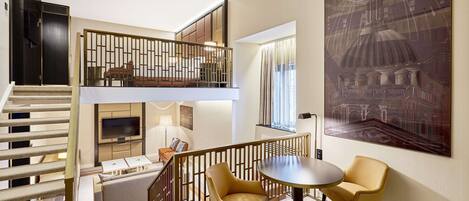 A modern interior with a staircase, a dining area with two chairs, a TV, and a large painting.