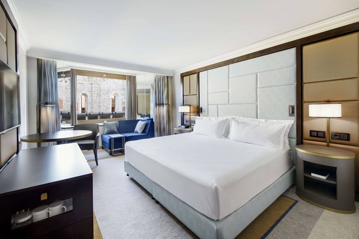 Une chambre d’hôtel avec un grand lit, un bureau, une chaise, un canapé et une vue sur un immeuble par la fenêtre.