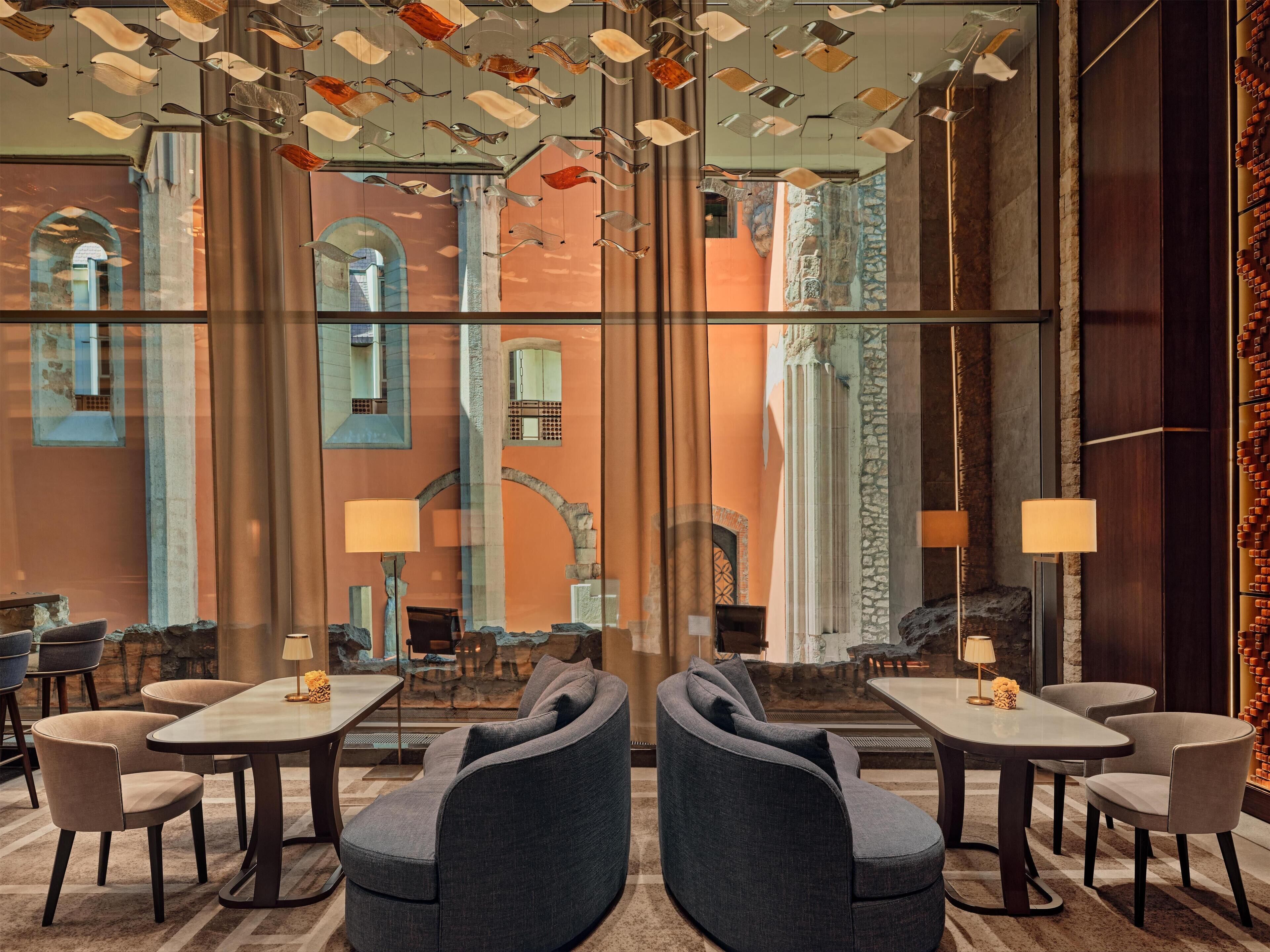 A modern interior with a glass wall reflecting an urban street view, a central dining table with chairs, and a unique ceiling light fixture.