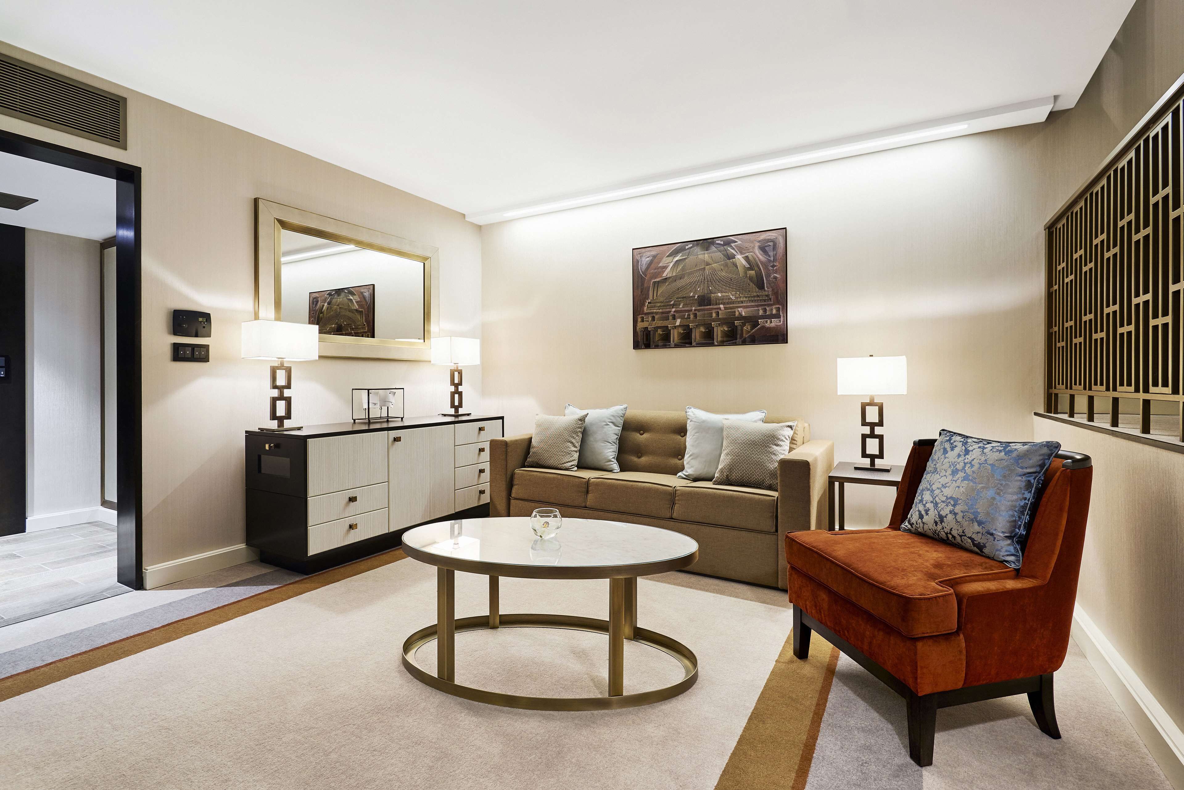 A modern living room with a round coffee table, a sofa, a brown armchair, and a side table with lamps.