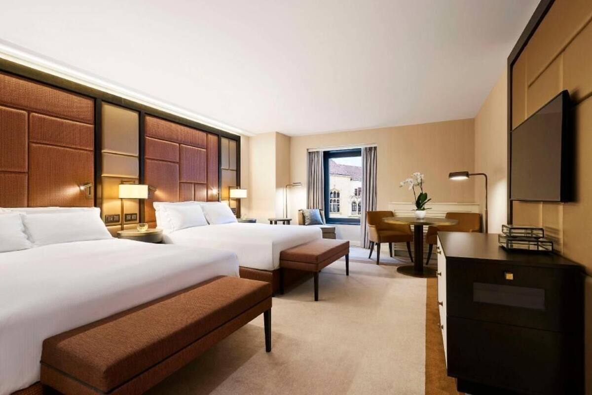 Une chambre d’hôtel avec deux lits, un bureau, une chaise, une télévision et une fenêtre donnant sur un paysage agréable.